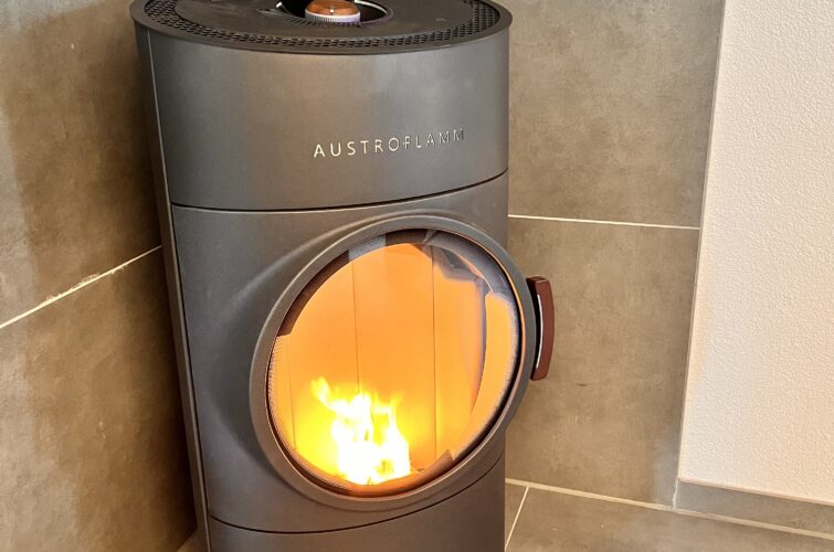 Pelletofen Clou von Austroflamm in anthrazit, brennend in einer Zimmerecke.